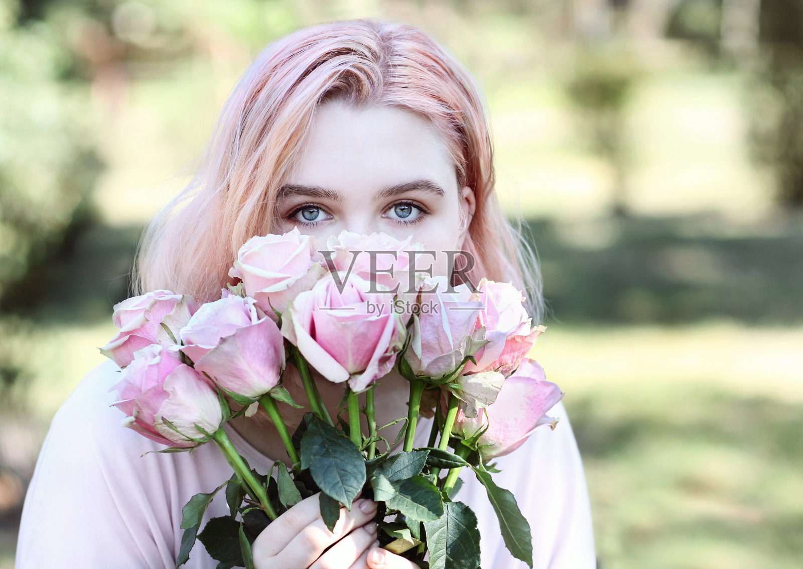 漂亮的蓝眼睛女孩闻着粉红色的玫瑰。照片摄影图片