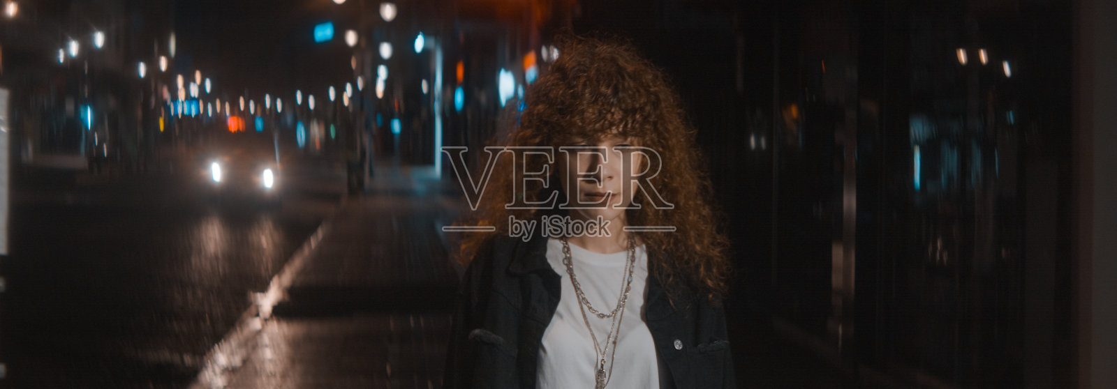 穿着白色t恤和黑色夹克的卷发女人在夜晚走在大街上，穿着变形喇叭裤和城市灯光——时尚的服装和女权主义的概念照片摄影图片