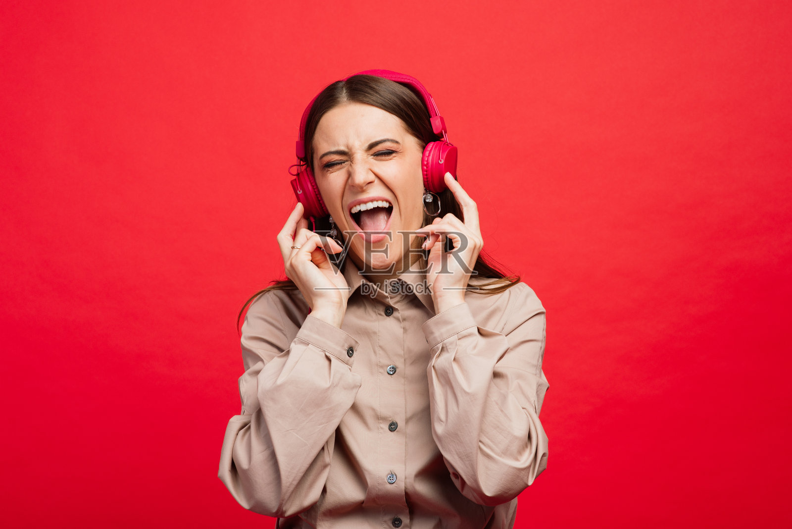 一个情绪化的白人女人戴着耳机在红色背景下听音乐照片摄影图片