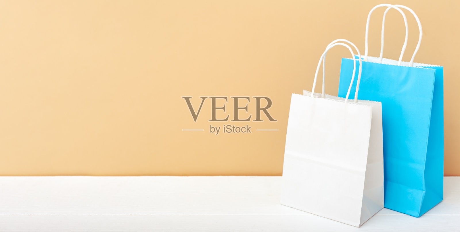 蓝白工艺纸袋。购物模型袋纸包白色桌子米色灯光背景与拷贝空间。购物、销售、送餐服务。长网页横幅拷贝空间照片摄影图片