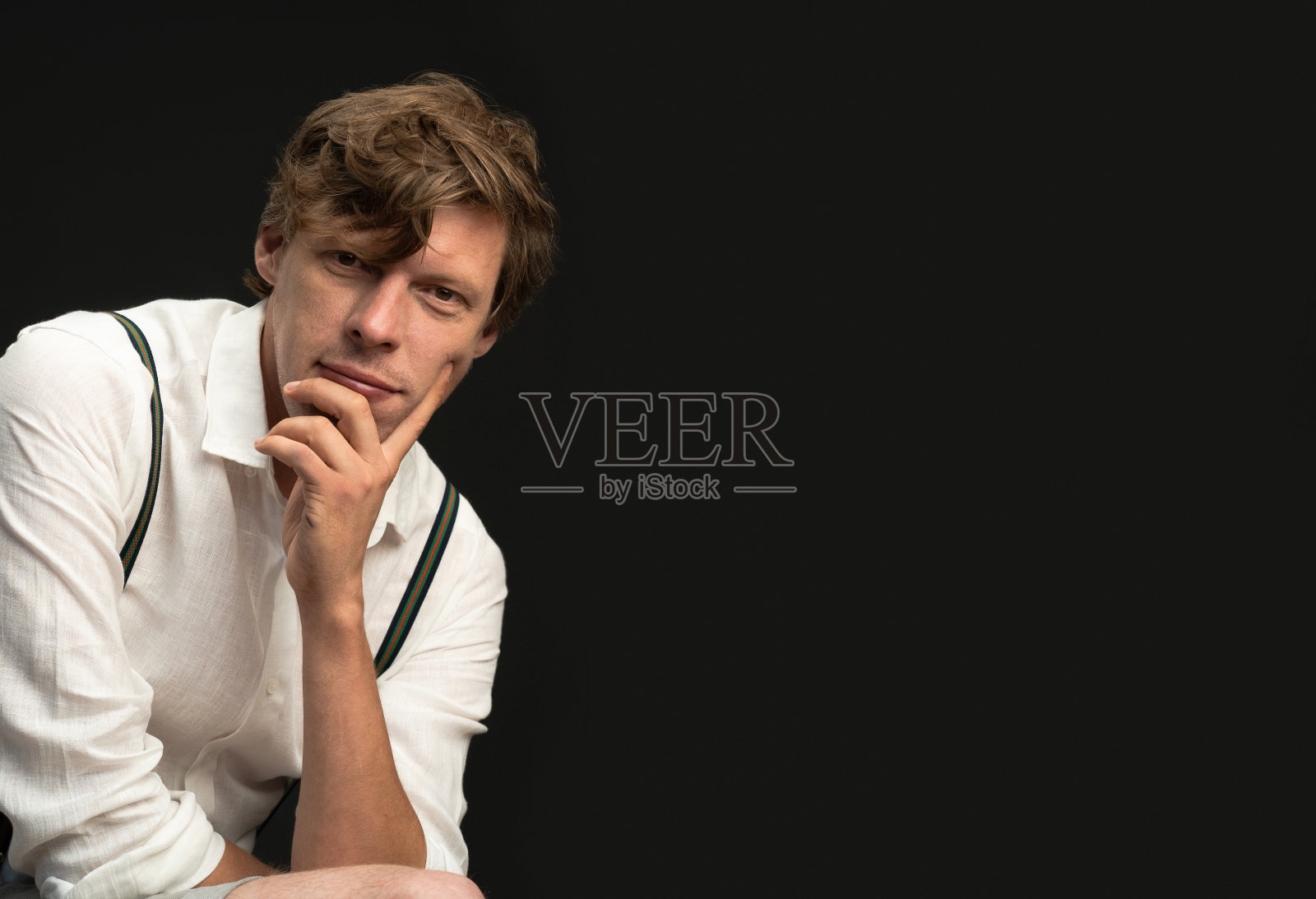 一个穿着白衬衫的深思熟虑的男人在黑色的背景下看着相机。文本空白照片摄影图片