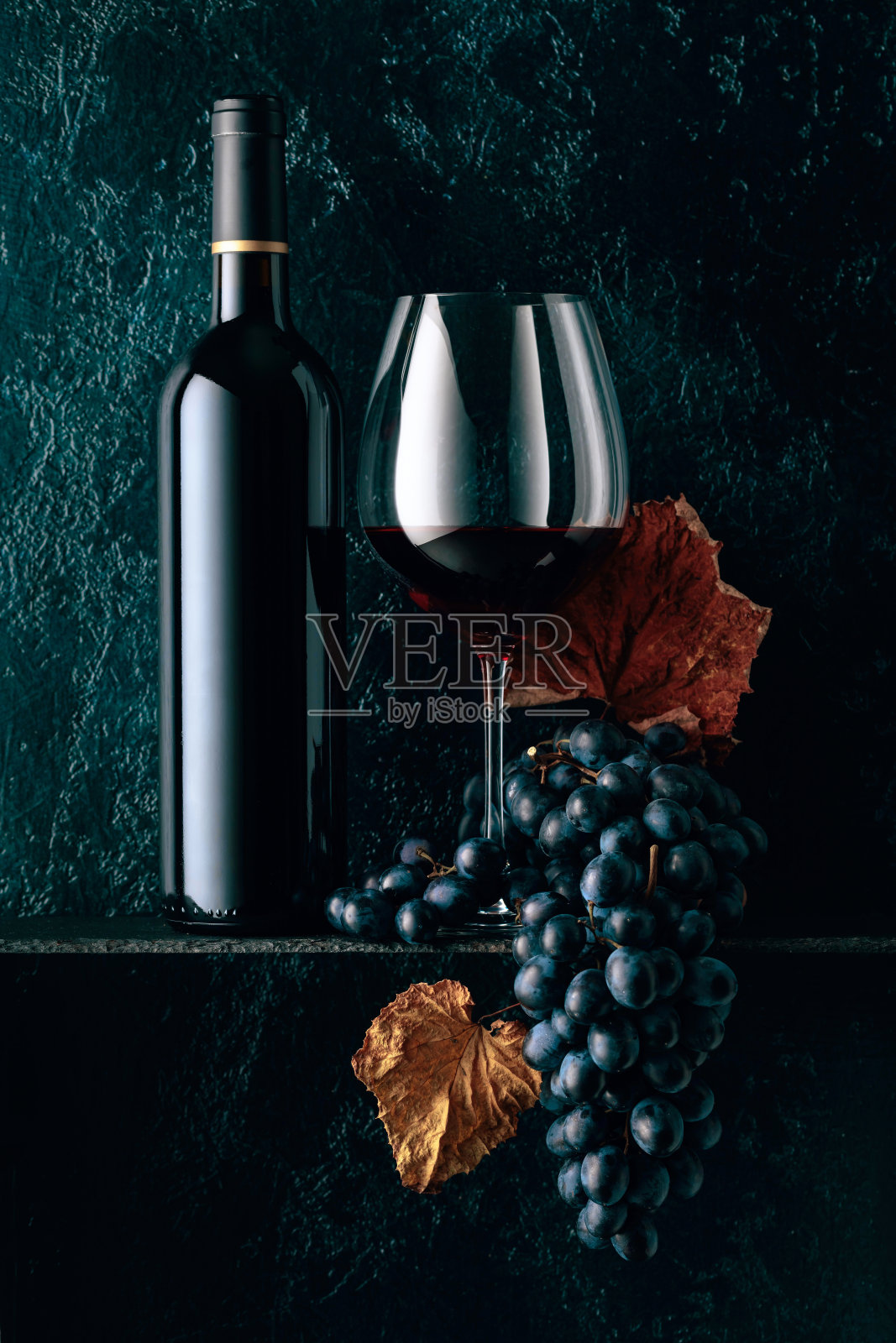 红酒和蓝色的葡萄与干燥的藤叶在一个古老的深蓝色背景。照片摄影图片