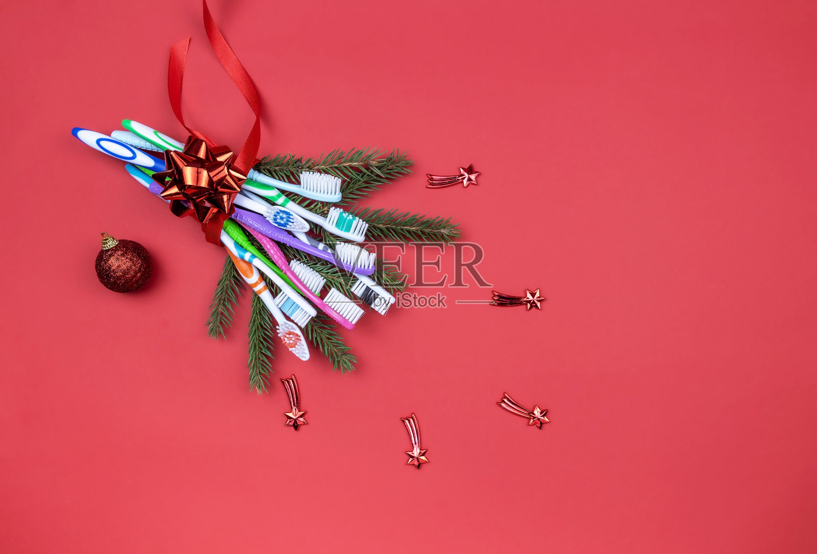 一束用彩带系在红色背景上的牙刷和云杉树枝照片摄影图片