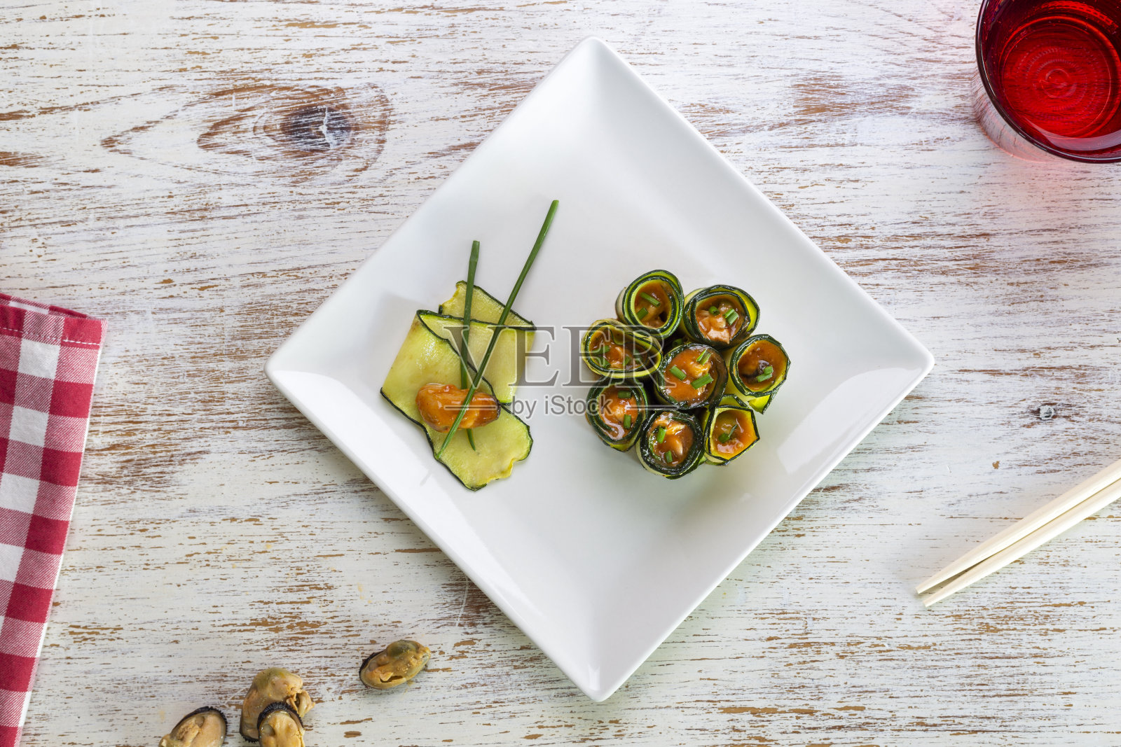 餐厅白色的桌子上，方形的白色盘子上放着几卷腌西葫芦和贻贝照片摄影图片