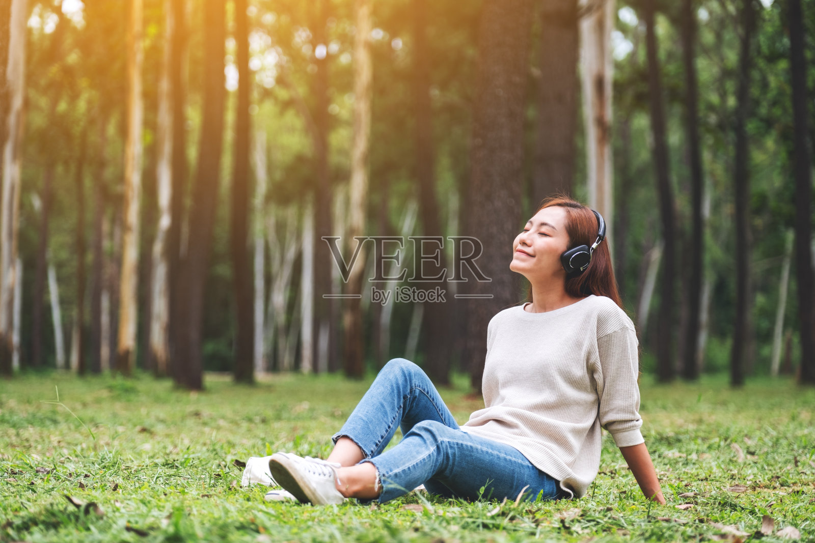 一位年轻的亚洲女子喜欢戴着耳机在公园里听音乐，心情舒畅照片摄影图片
