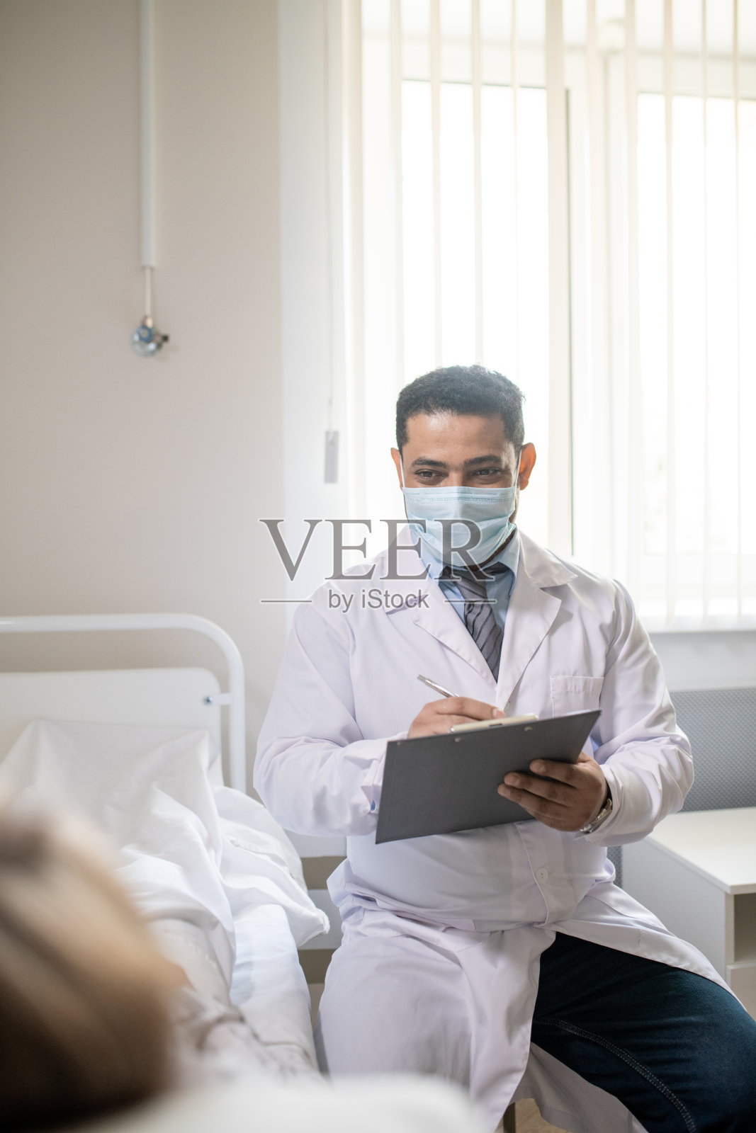 年轻男医生穿着正装，白大褂，戴着防护面具做记录照片摄影图片