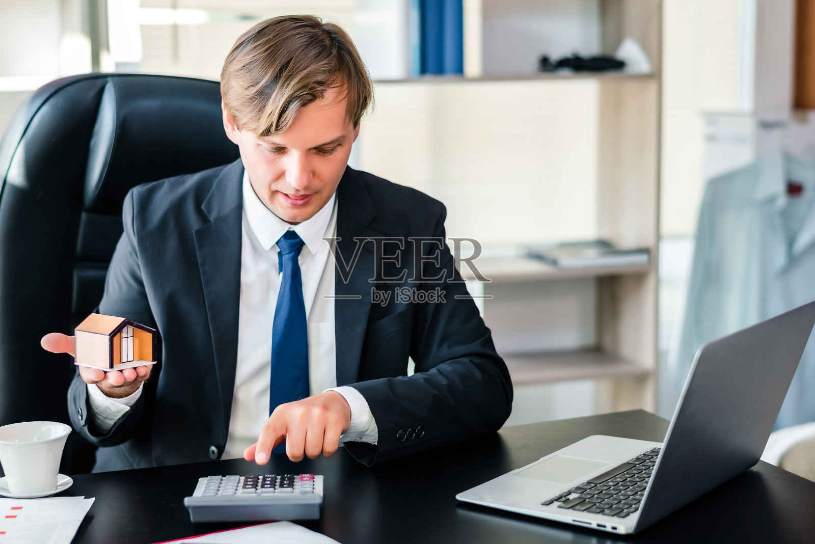 幸福商人手中拿着房子的模型在办公，房地产置业投资或销售或金融贷款的概念照片摄影图片
