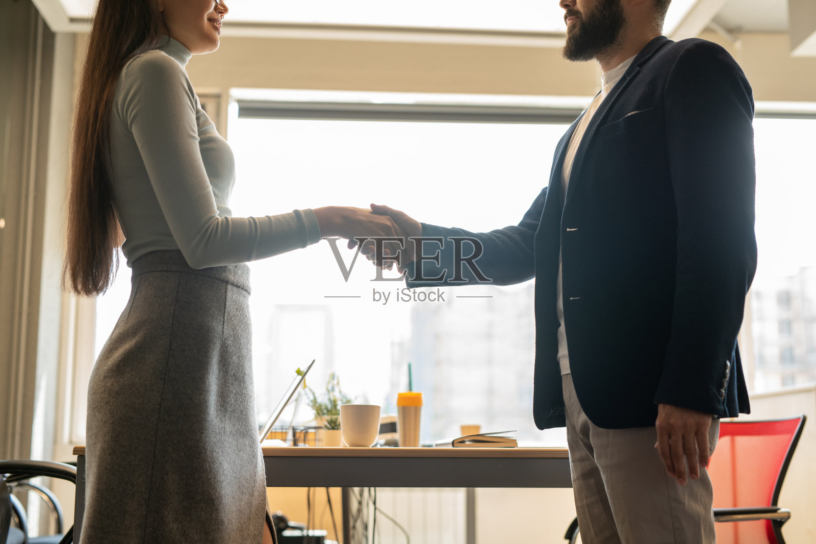 侧面的两个年轻的同事在休闲服握手对着窗户照片摄影图片