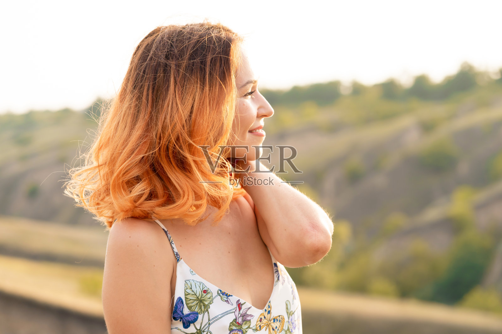 温柔美丽的红发女孩欣赏日落在一个小山的田野。照片摄影图片