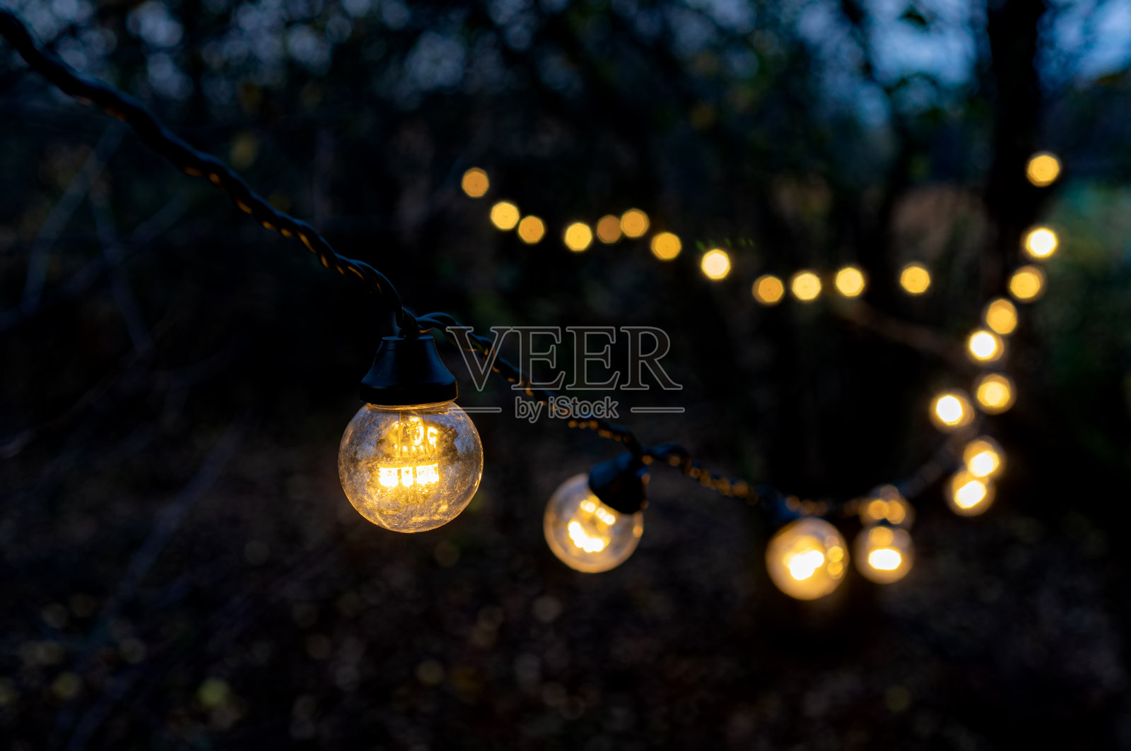 圣诞花环灯悬挂在花园里。暖白色的颜色。照片摄影图片