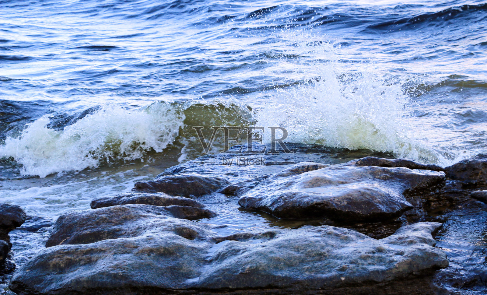 海浪冲上海岸，撞击岩石，在海岸附近产生许多水花和水花。在暴风雨的天气里，在带有泡沫和溅起水花的石头海岸附近的河上冲浪。照片摄影图片