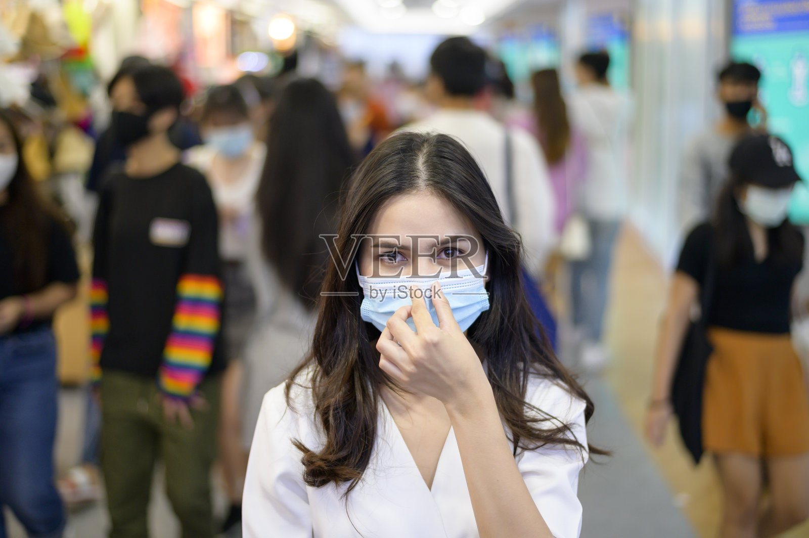 在新冠肺炎大流行、新冠肺炎防护、安全生活方式理念下，一名妇女戴着防护口罩走在人群密集的街道上照片摄影图片