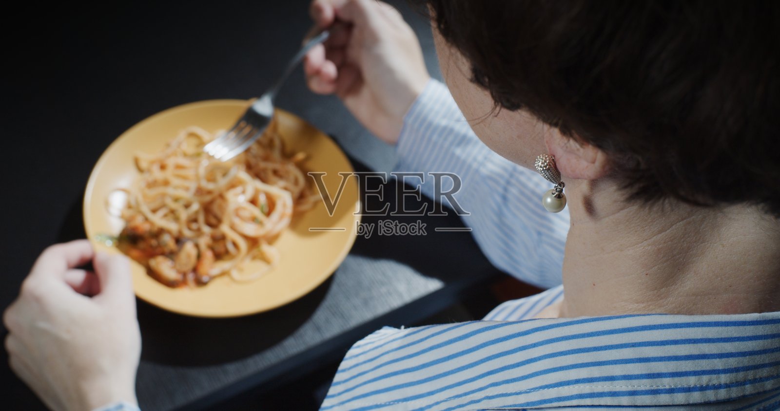 越过肩膀，一个成熟的女人坐在桌子上吃着海鲜意大利面照片摄影图片