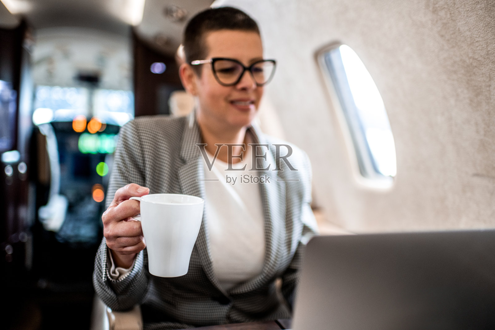 女商人端着茶，在商务飞机上用笔记本电脑工作照片摄影图片
