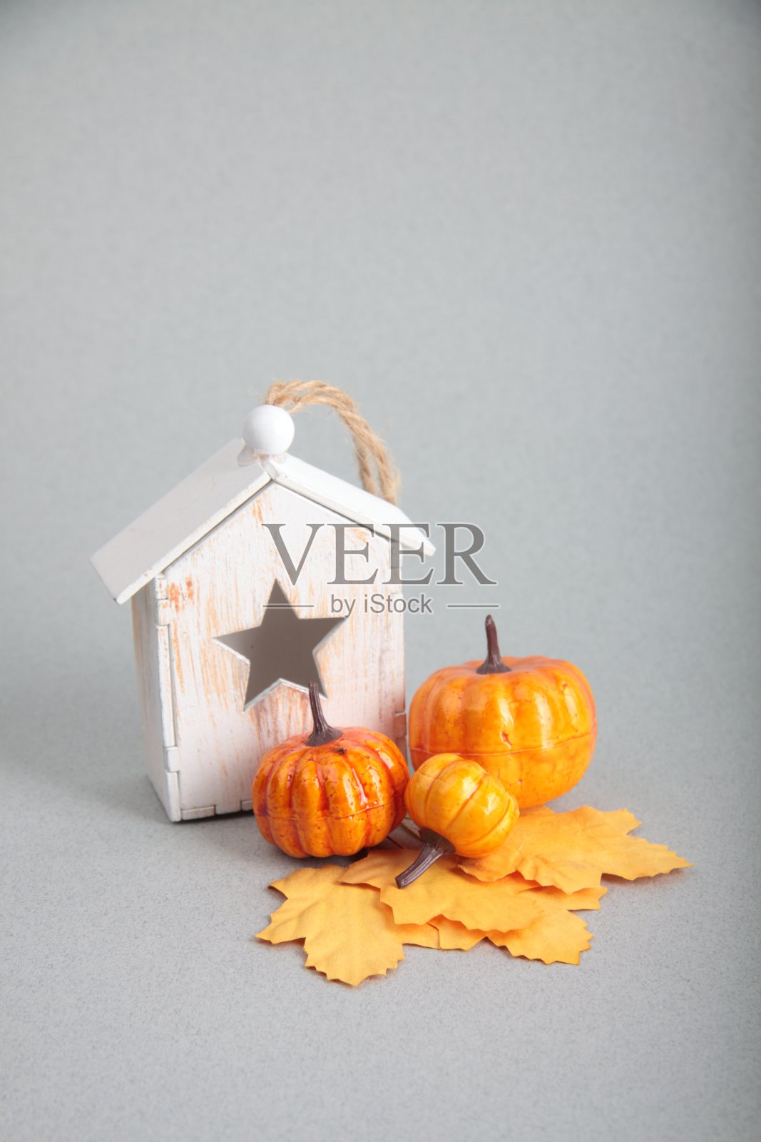 木制的玩具房子，黄色的秋叶和南瓜在灰色的背景。Hygge概念照片摄影图片