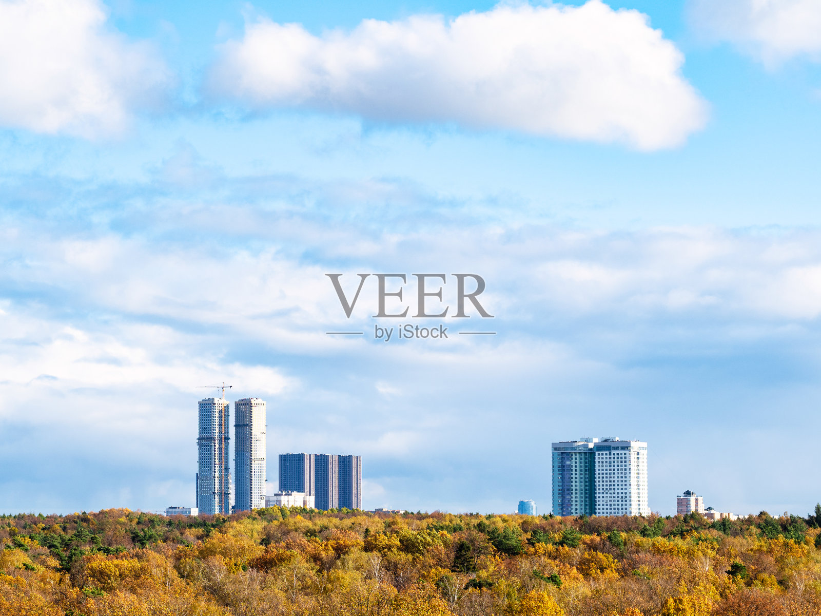 蓝色的天空，黄色的森林和房屋上有云朵照片摄影图片