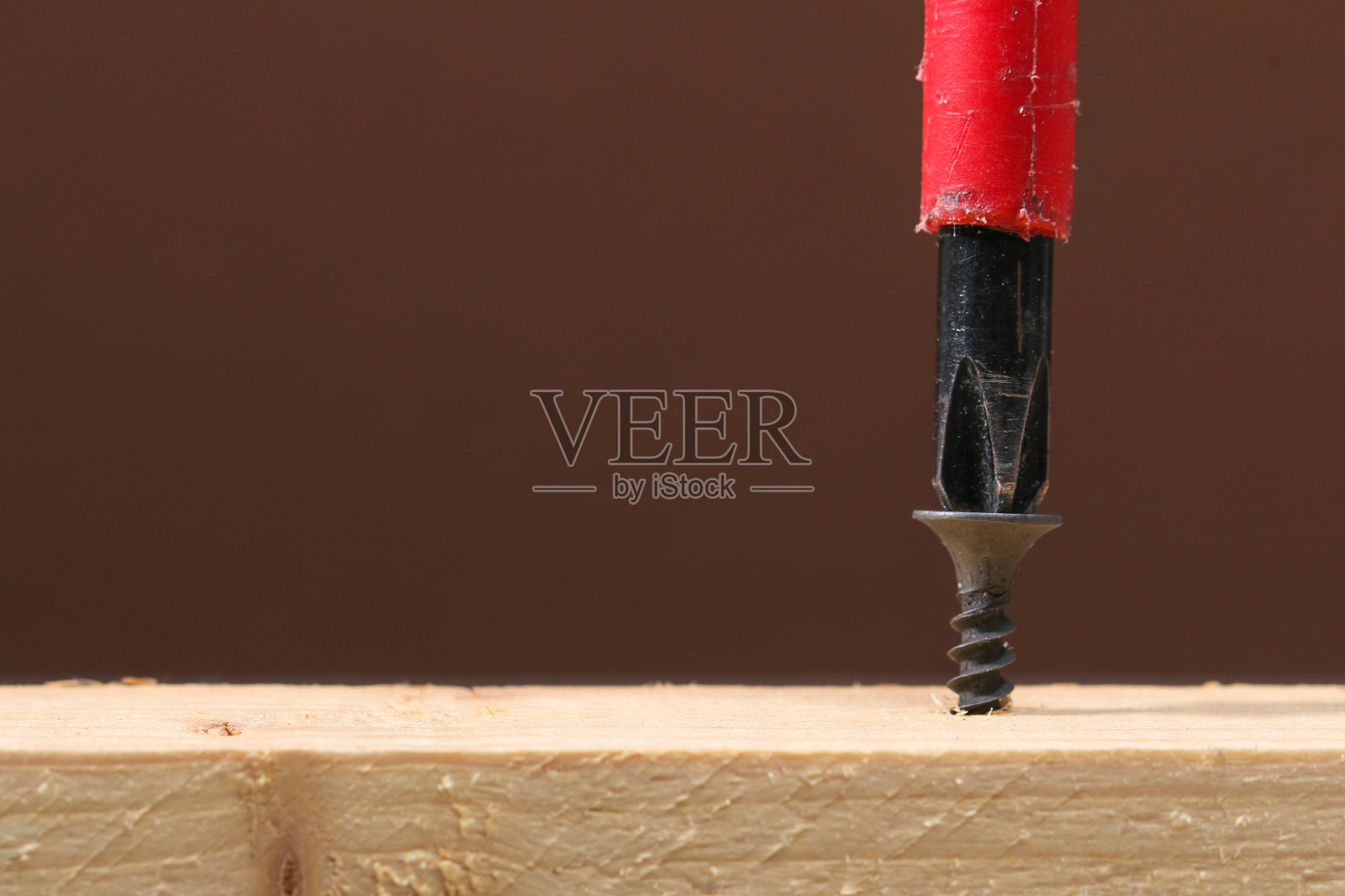 用螺丝刀把黑铁螺丝拧进木头里。紧固件和硬件。照片摄影图片