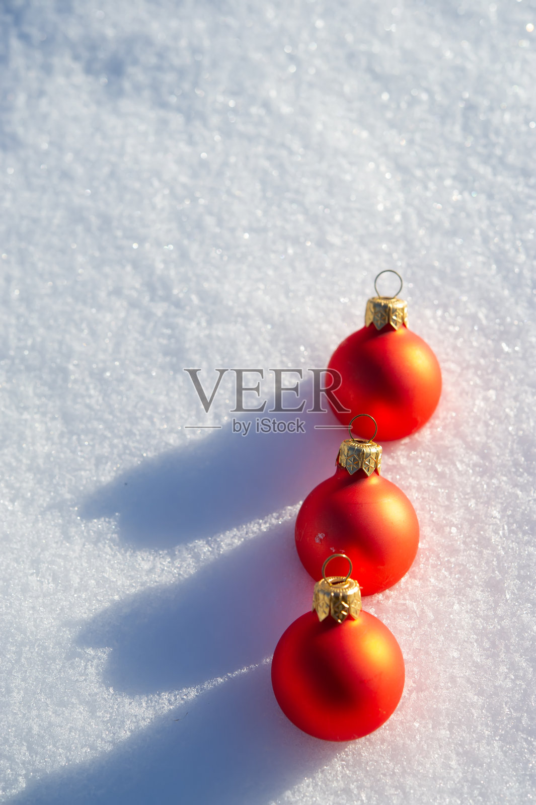 阳光明媚的日子里，雪地上的红色圣诞球。照片摄影图片
