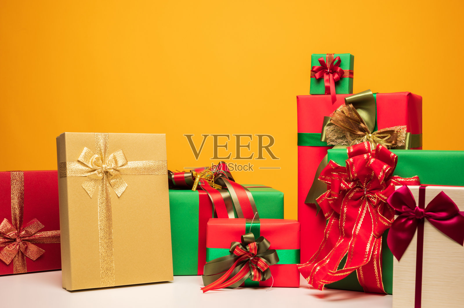 许多礼盒的样品包装装饰蝴蝶结丝带。一大堆的礼品堆在黄色的底色上。圣诞快乐，新年快乐的节日概念。照片摄影图片