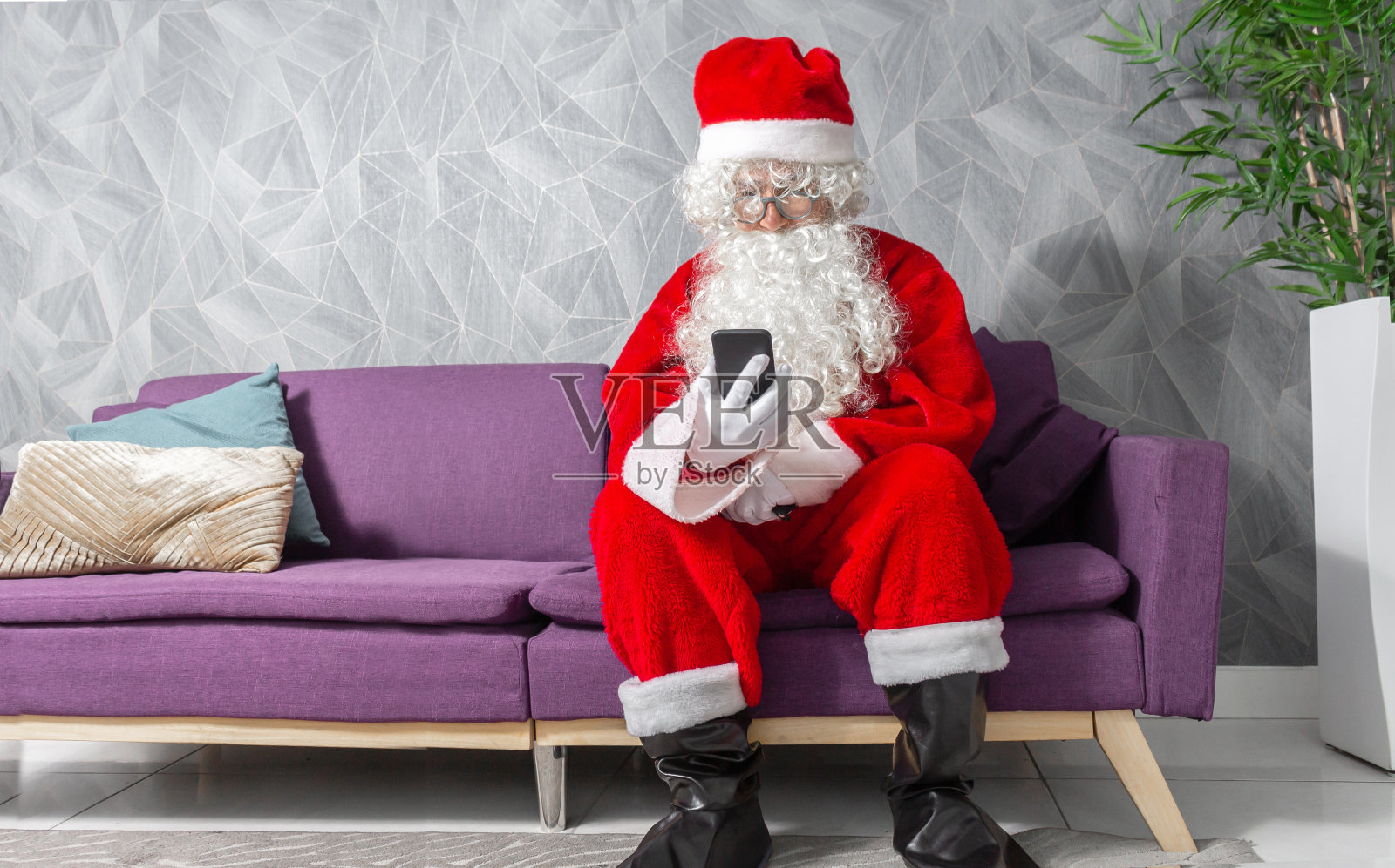 圣诞老人坐在沙发上看他的手机照片摄影图片