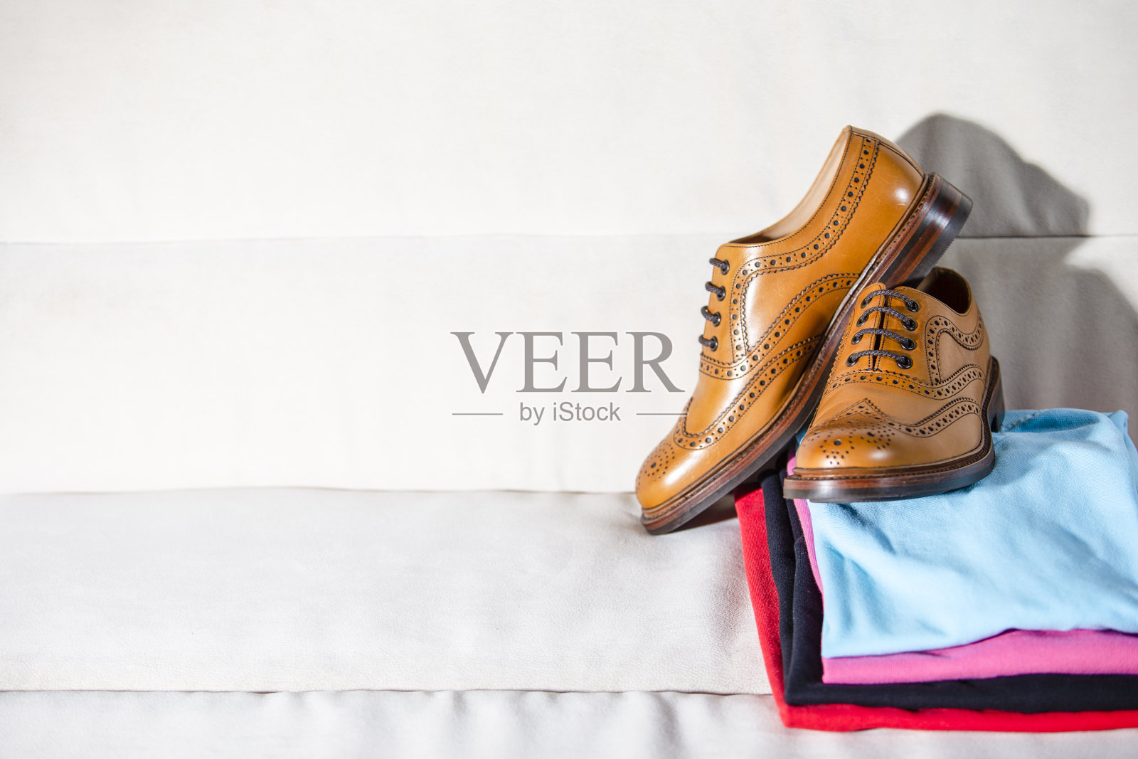 一对男性全brogues棕色牛津鞋放在一堆彩色衣服的特写。水平的作文照片摄影图片