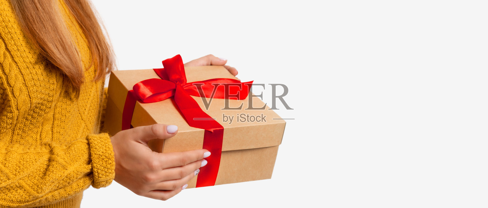 女性手中正拿着用红色蝴蝶结装饰的工艺品礼盒圣诞、新年。孤立的副本空间。一个穿着舒适温暖的黄色毛衣没有脸的女人。光背景横幅照片摄影图片