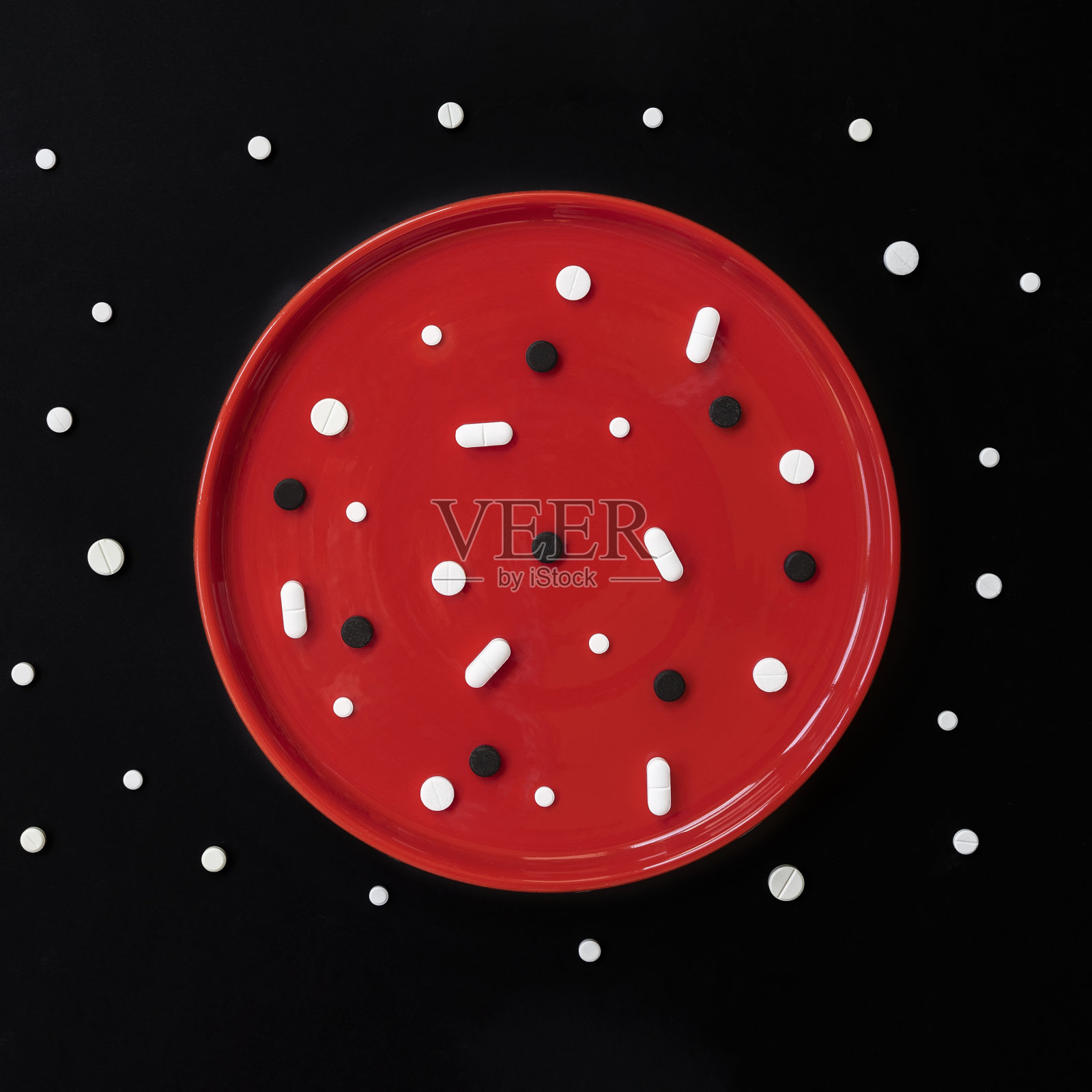 红色的盘子里有白色和黑色的药丸，正确使用药物的概念，不同的药物，片剂，药物，胶囊的健康。医学背景简介照片摄影图片