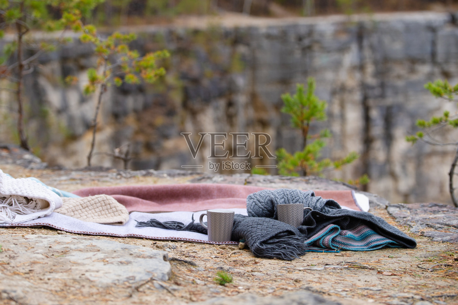 一条毯子，一件针织品和两个杯子躺在山的边缘。照片摄影图片