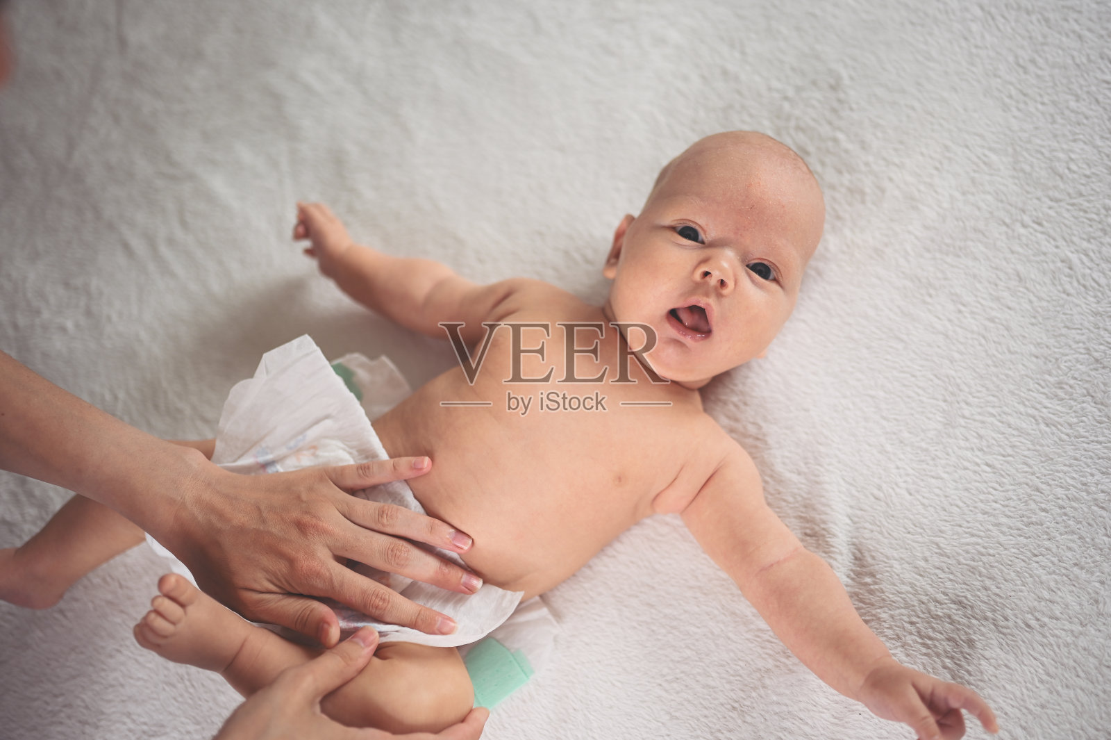 妈妈正在给躺在婴儿床上的可爱的、情绪化的、有趣的新生小男孩换尿布照片摄影图片