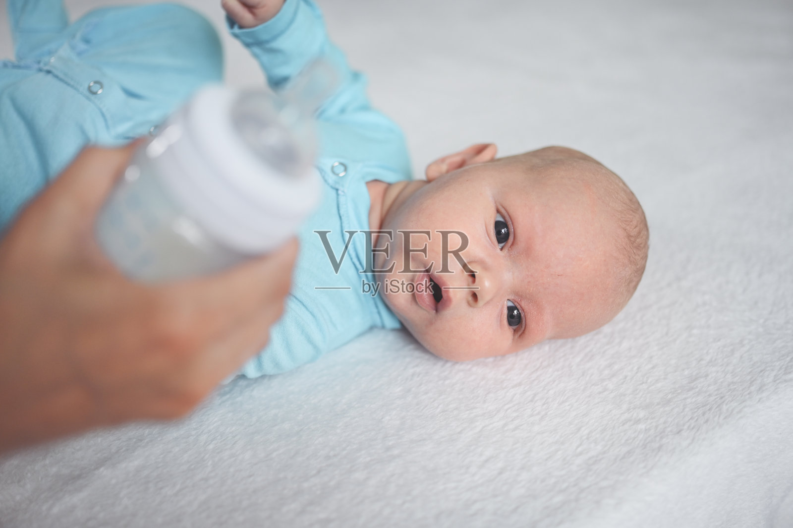 可爱的情感搞笑的新生男婴躺在床上拿着奶瓶。婴儿的面部表情。照片摄影图片