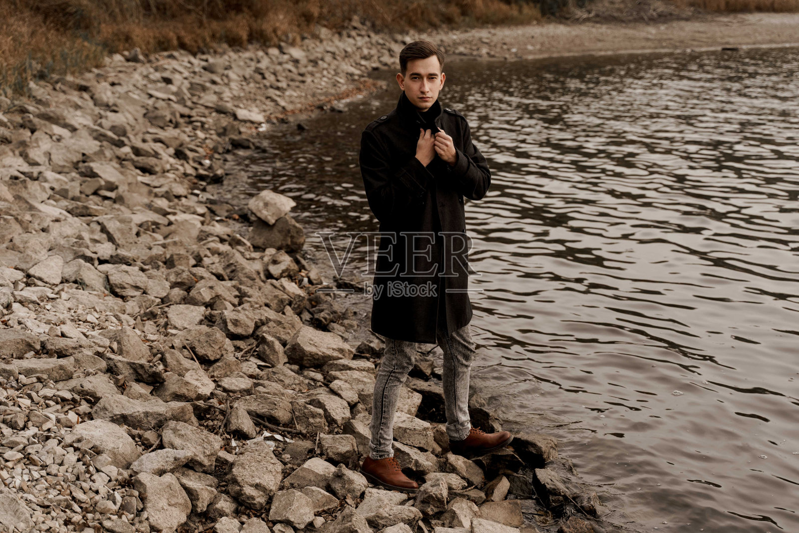 在隔离期间，自信的商人在湖边散步，思考他的生意。英俊的男士穿着正式的黑色外套照片摄影图片