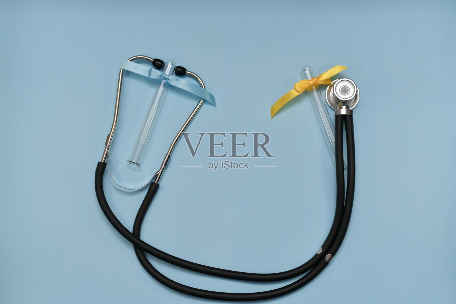 一个医用听诊器在浅蓝色的背景上，有两个试管，浅蓝色和黄色。照片摄影图片