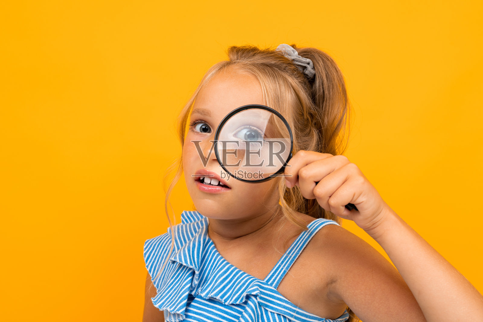 金发女孩透过放大镜看黄色背景照片摄影图片