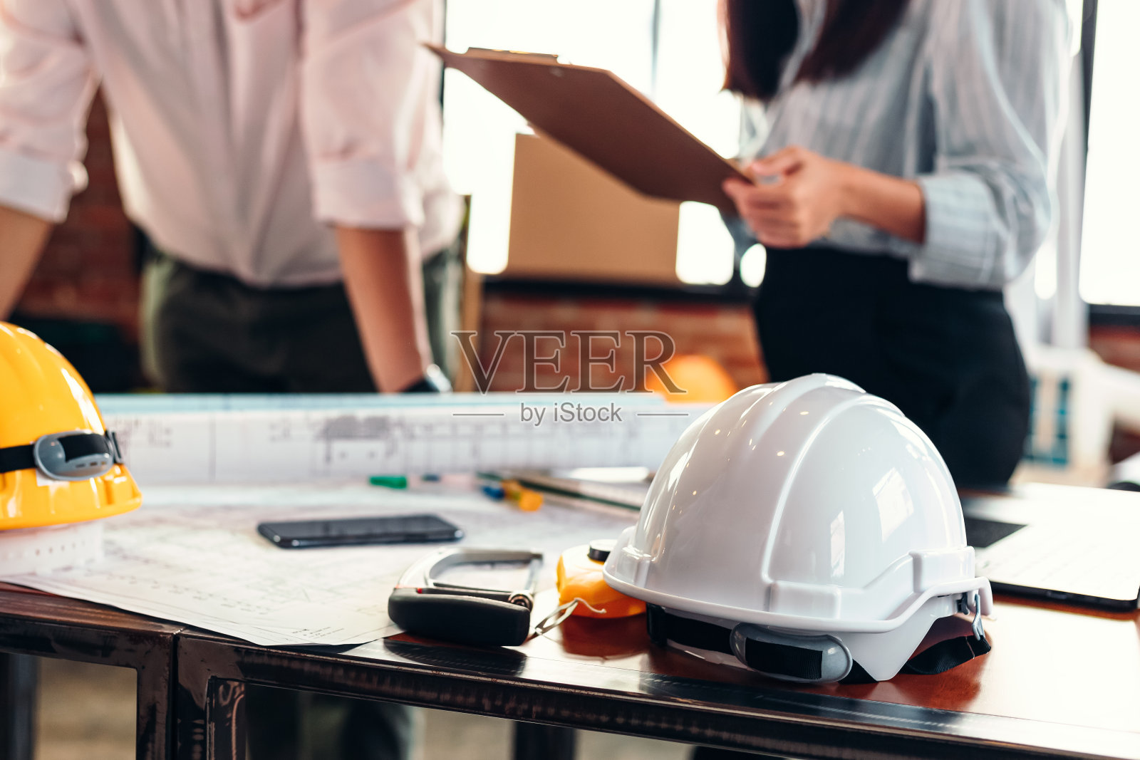 现场施工时将安全帽放在桌子上。建筑师，工程师和商人阅读规划背景。照片摄影图片