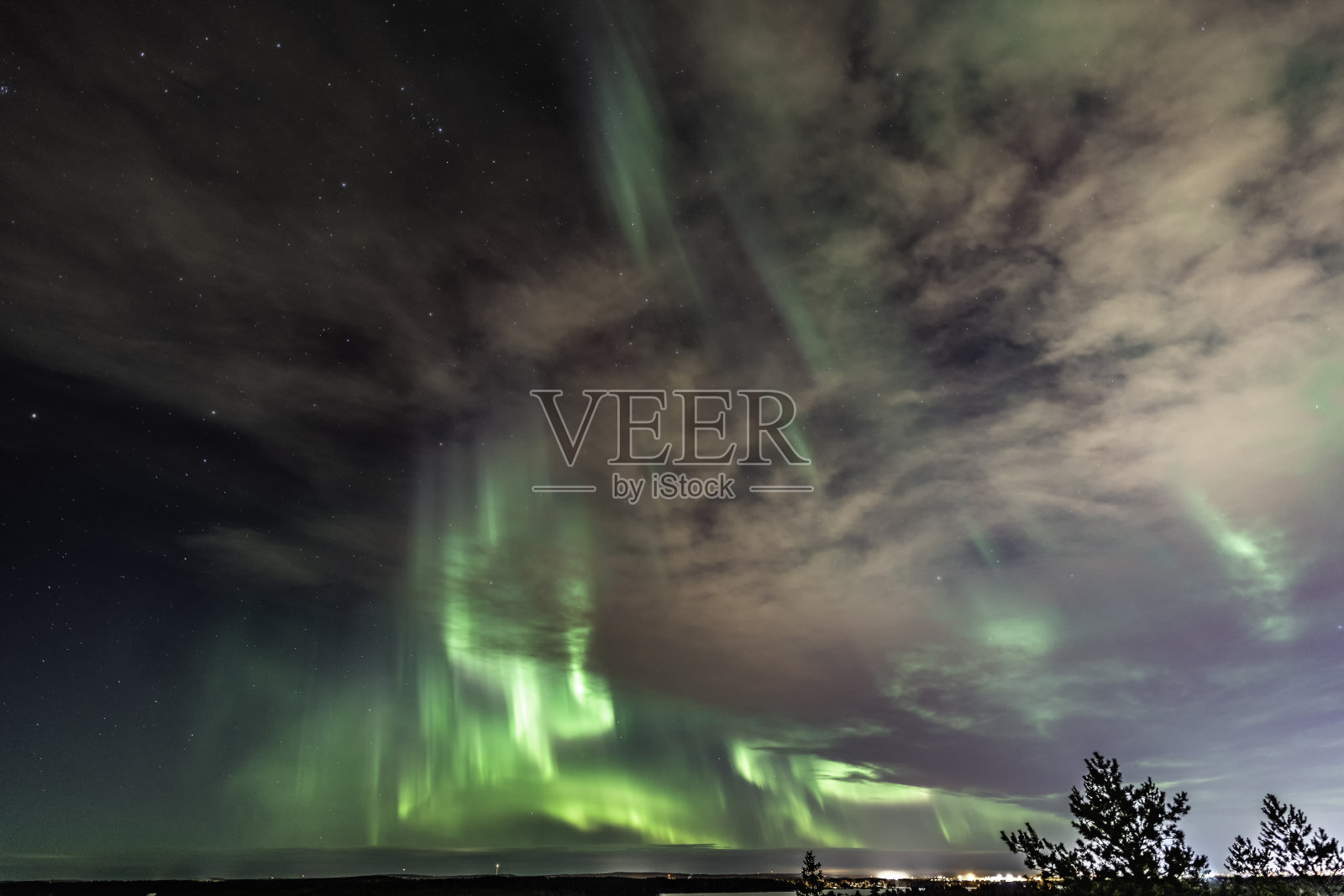 极光在晴朗的天空和云照耀着北欧乡村，绿色的北极光带向上指向，冬天的时间照片摄影图片