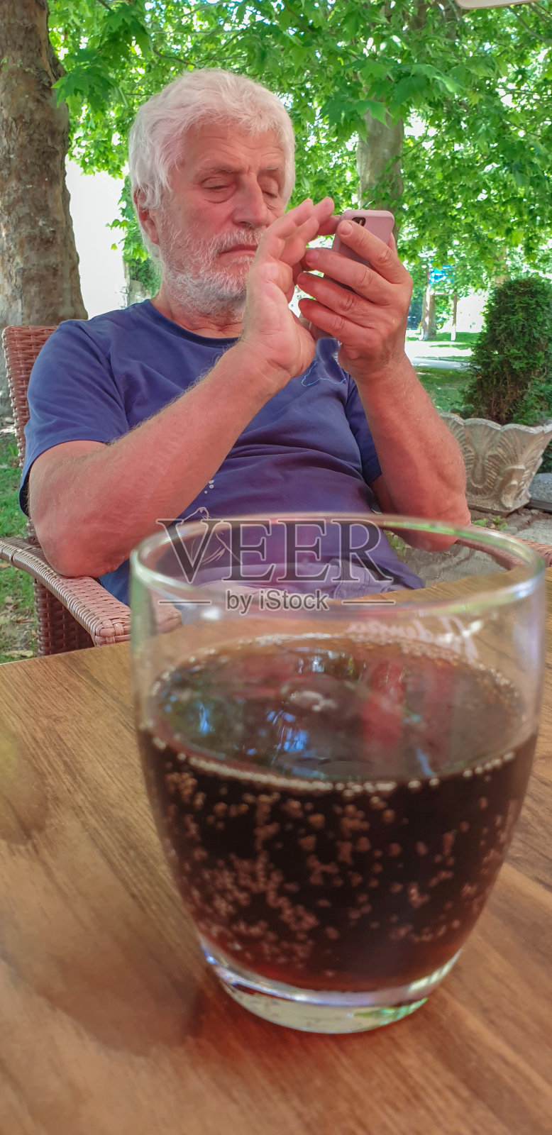 老人拿着手机和一杯冷饮照片摄影图片