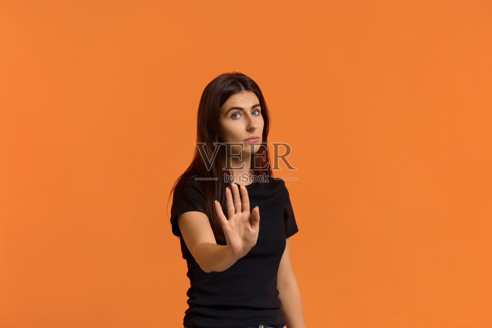 没有非法侵入。严肃的白人妇女在黑色t恤拉向相机看相机，显示停止手势，拒绝的东西。孤立在一堵橙色的墙上照片摄影图片