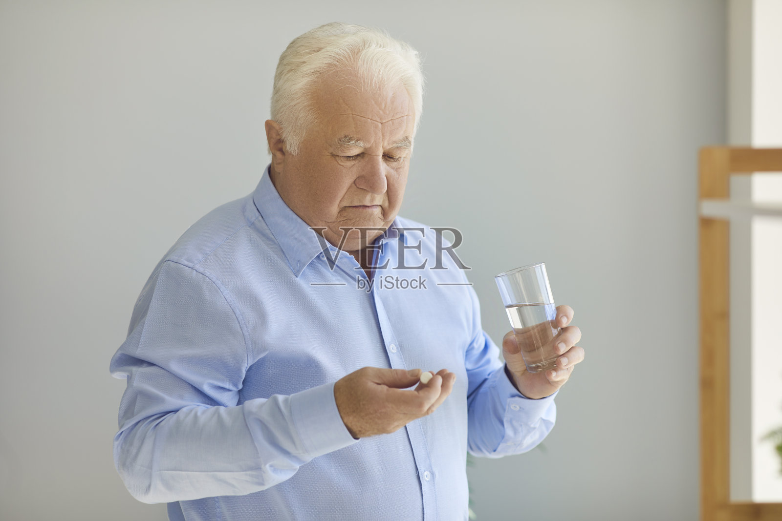 年长的男人拿着药丸和水杯，怀疑药物是否值得照片摄影图片