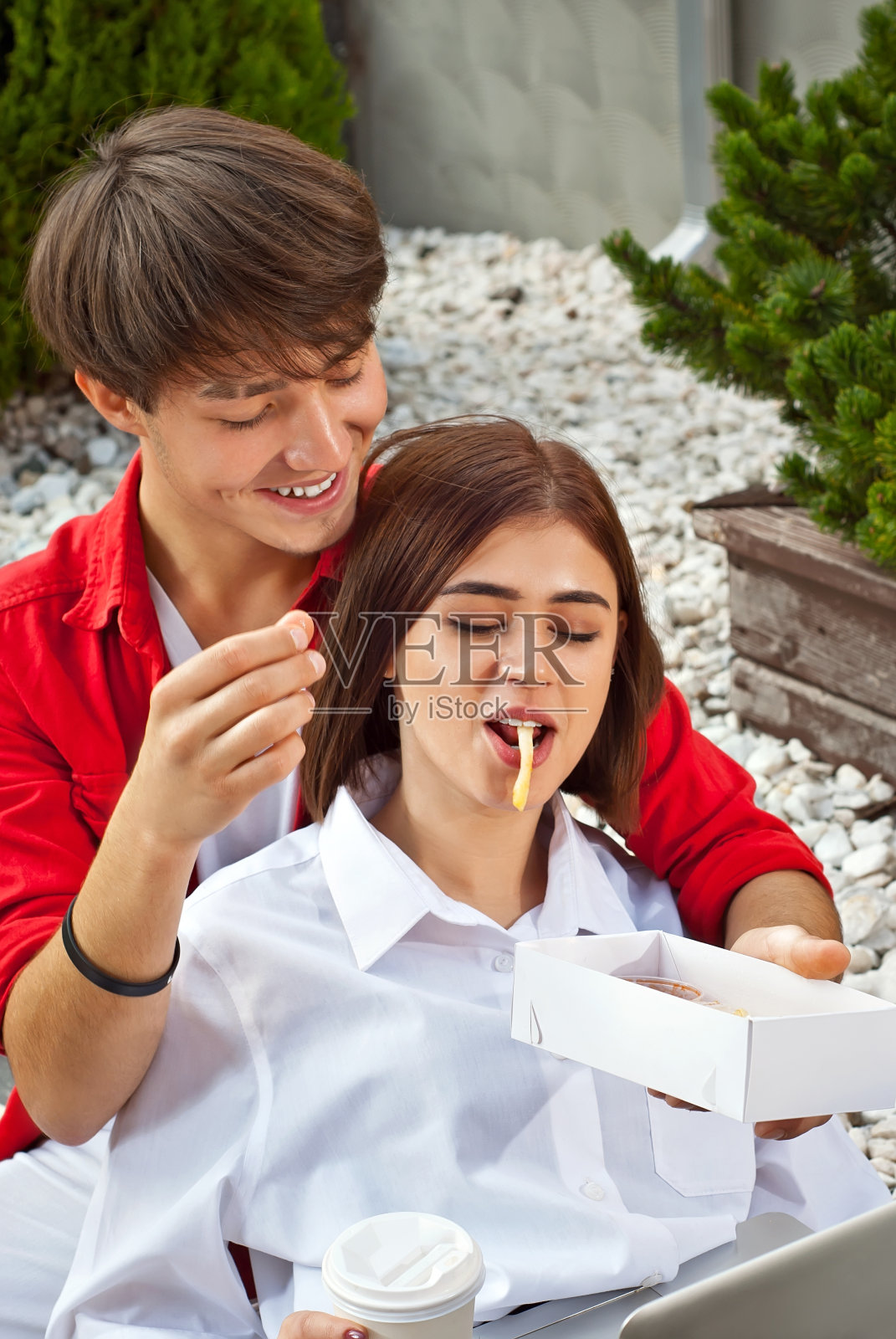 男人和女人一起在户外吃午饭。一对夫妇在吃薯条。快餐和街头小吃的概念。纸盒和一次性杯子里的食物。照片摄影图片