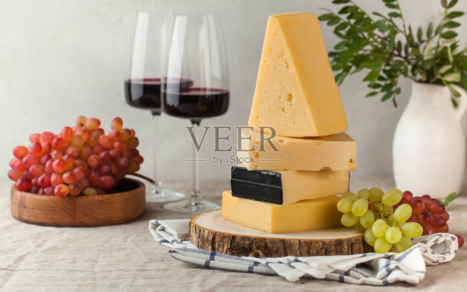 亚麻桌布上挂着各种各样的奶酪、葡萄和几杯红酒。照片摄影图片