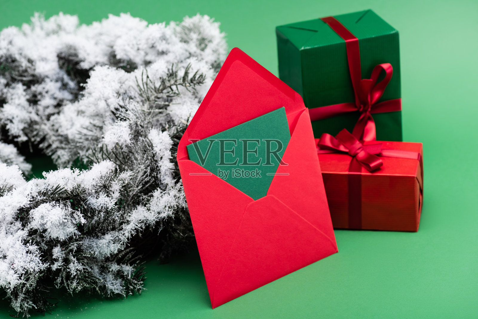 礼品盒旁边是带卡片的红色信封，绿色的树枝上装饰着雪照片摄影图片