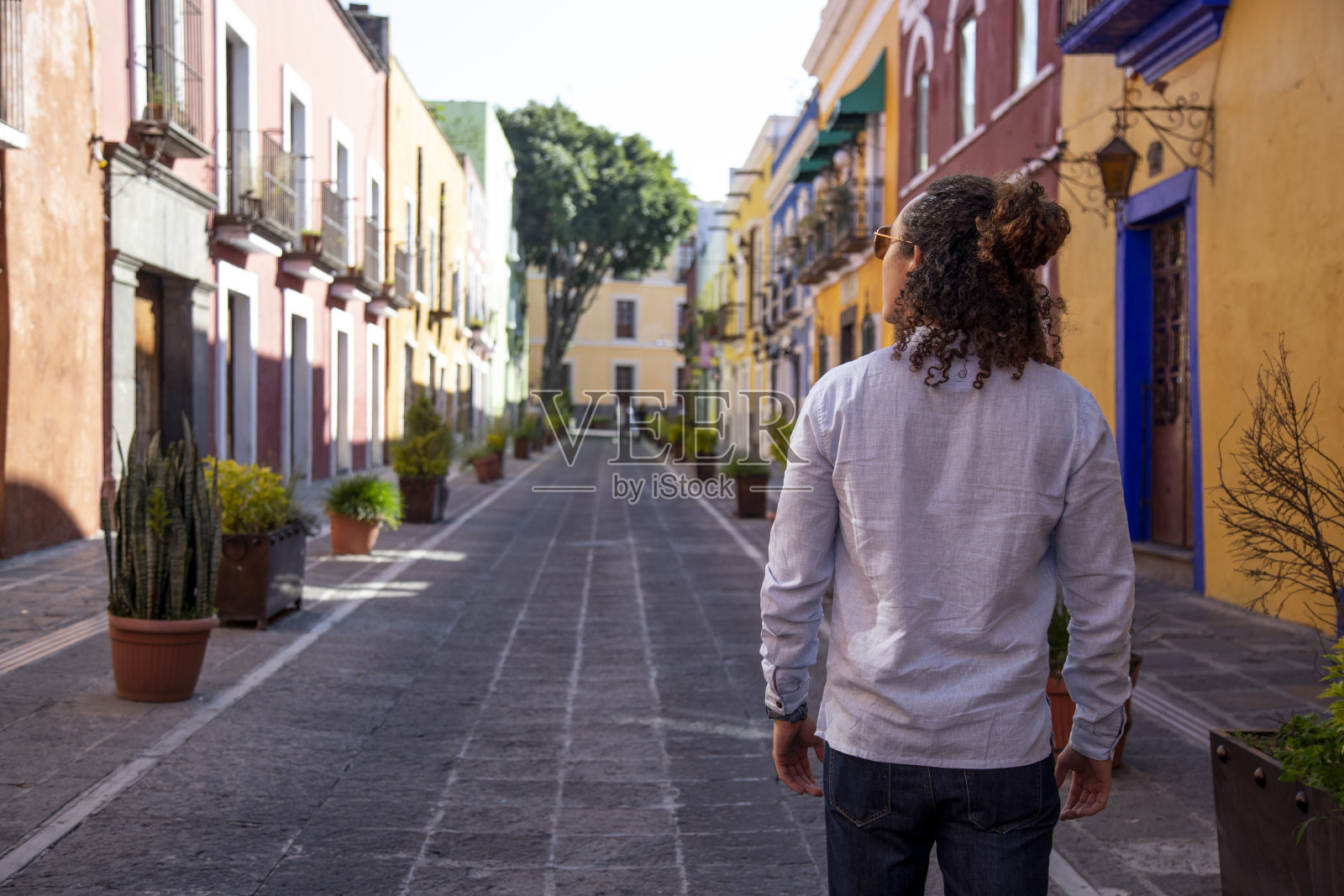 一名卷发男子走在普埃布拉五颜六色的殖民地街道上照片摄影图片