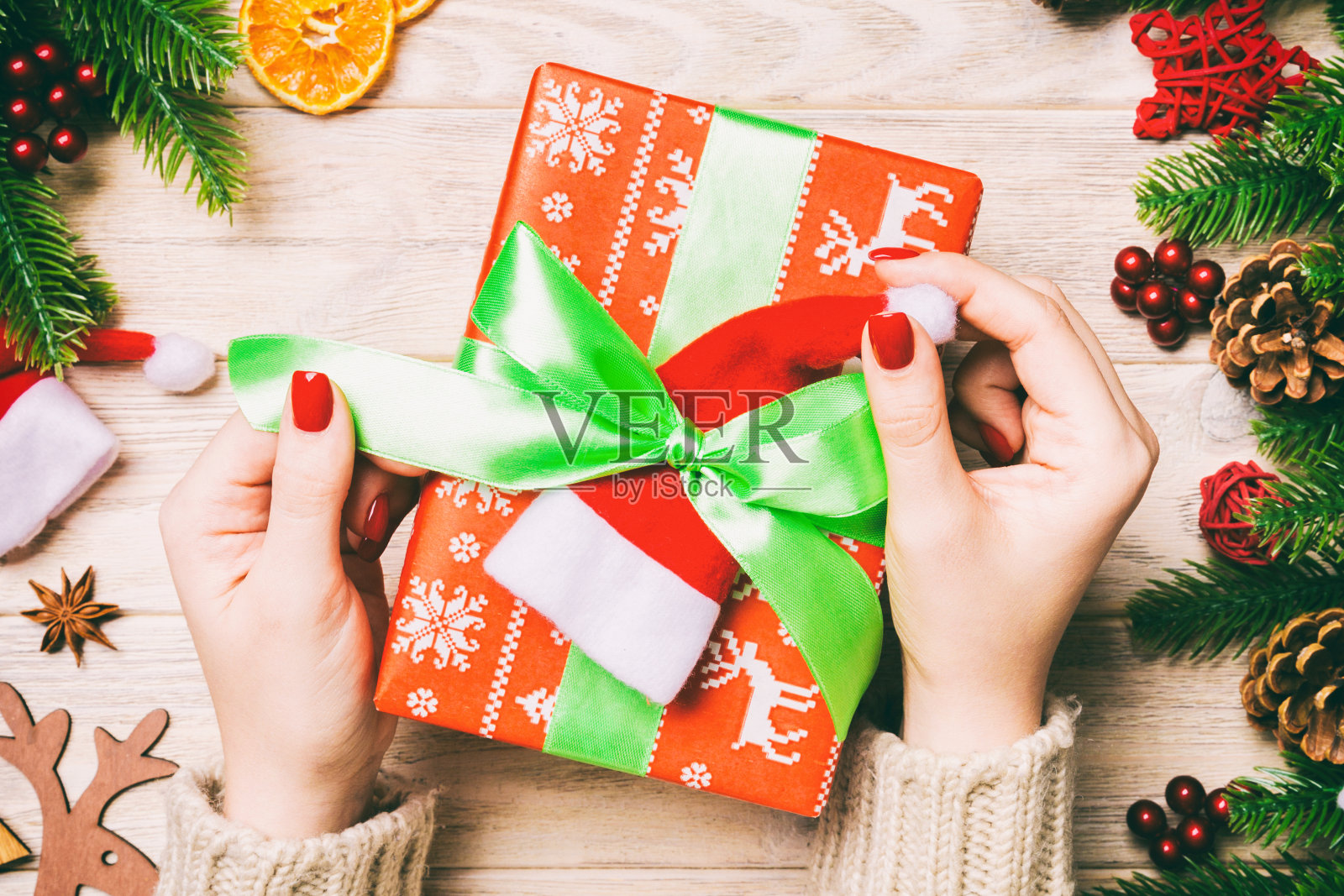 女性在节日木质背景上系新年礼物俯视图：冷杉树和节日装饰，圣诞节概念照片摄影图片