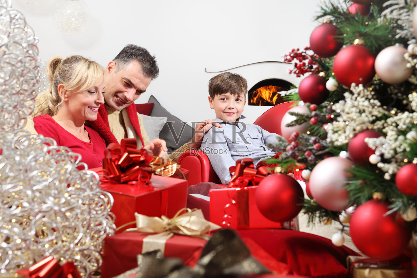 圣诞节快乐，幸福家庭在家中，父母在装饰好的圣诞树旁给孩子送礼物，一家人坐在客厅里，被壁炉温暖，喜笑颜开照片摄影图片