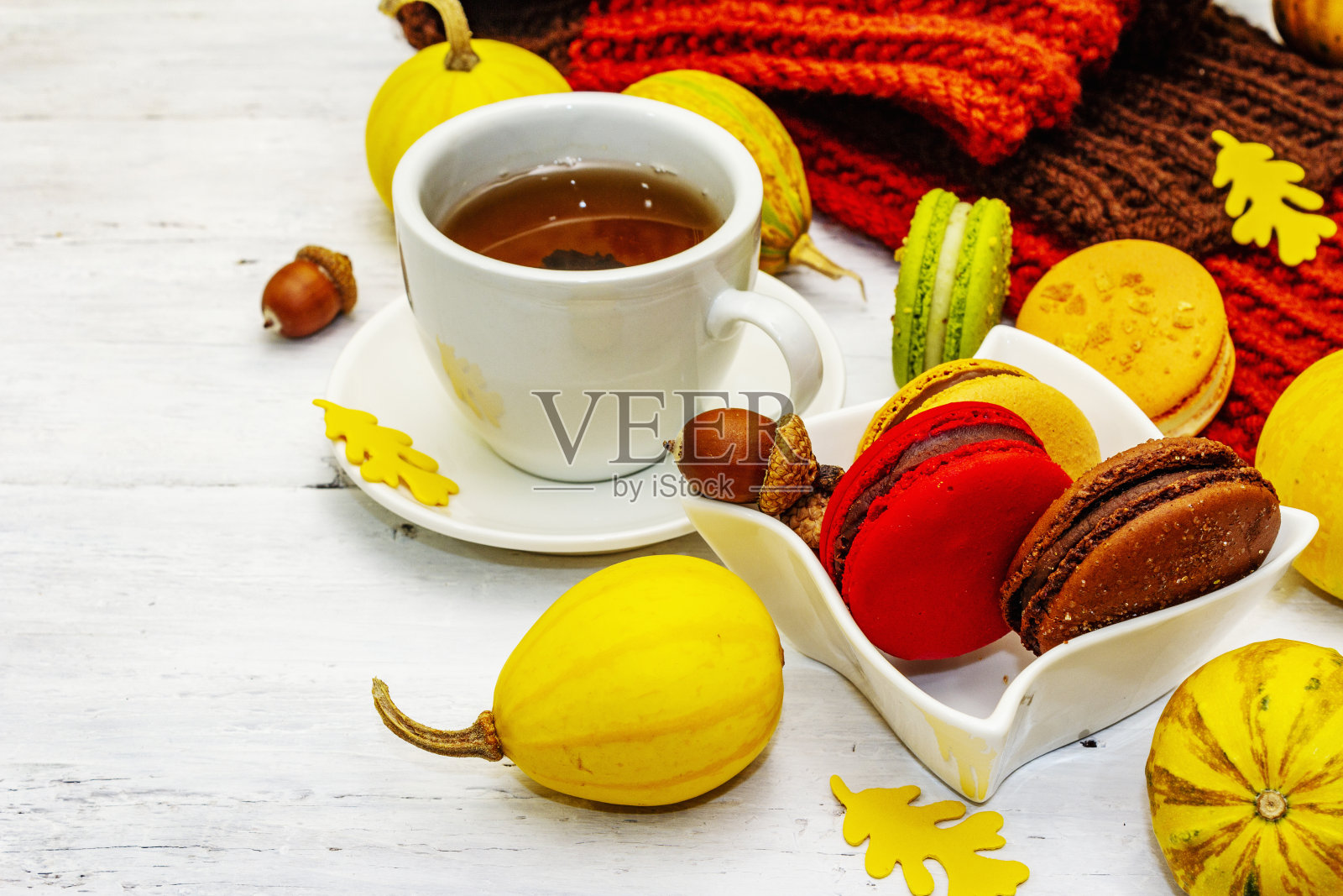 秋天的法式马卡龙配上热茶。万圣节甜点，感恩节菜单。装饰南瓜，围巾，落叶和橡子照片摄影图片