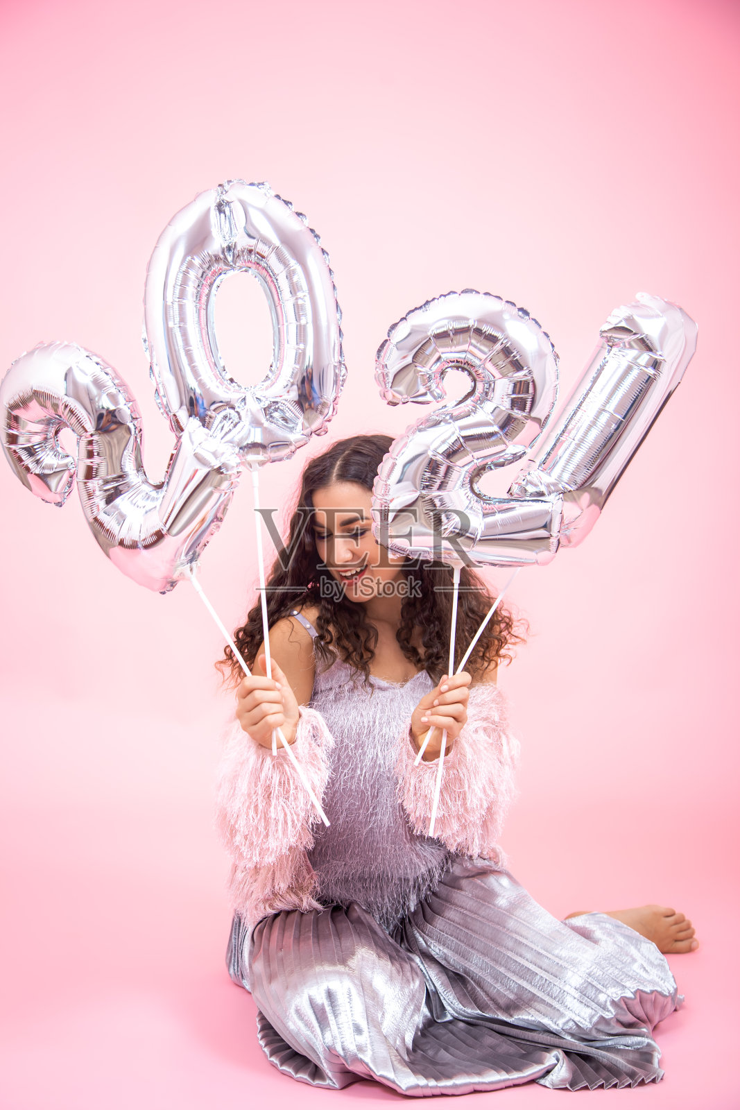 粉色背景上的女孩手里拿着银色气球，上面写着2021年的数字照片摄影图片