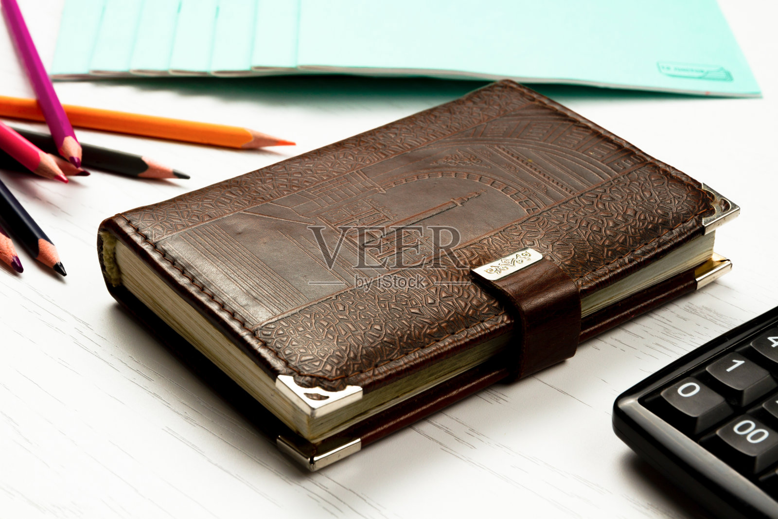 彩色铅笔和皮质日记本放在一张白色的木桌上照片摄影图片