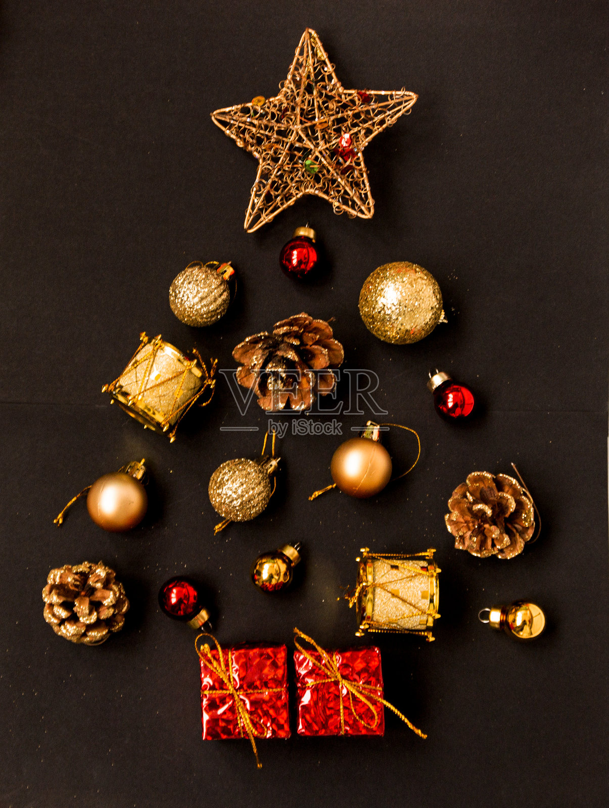 圣诞或新年圣诞树由金色和红色的球、星星、礼盒、鼓和冷杉球果在黑色背景上制作而成。照片摄影图片