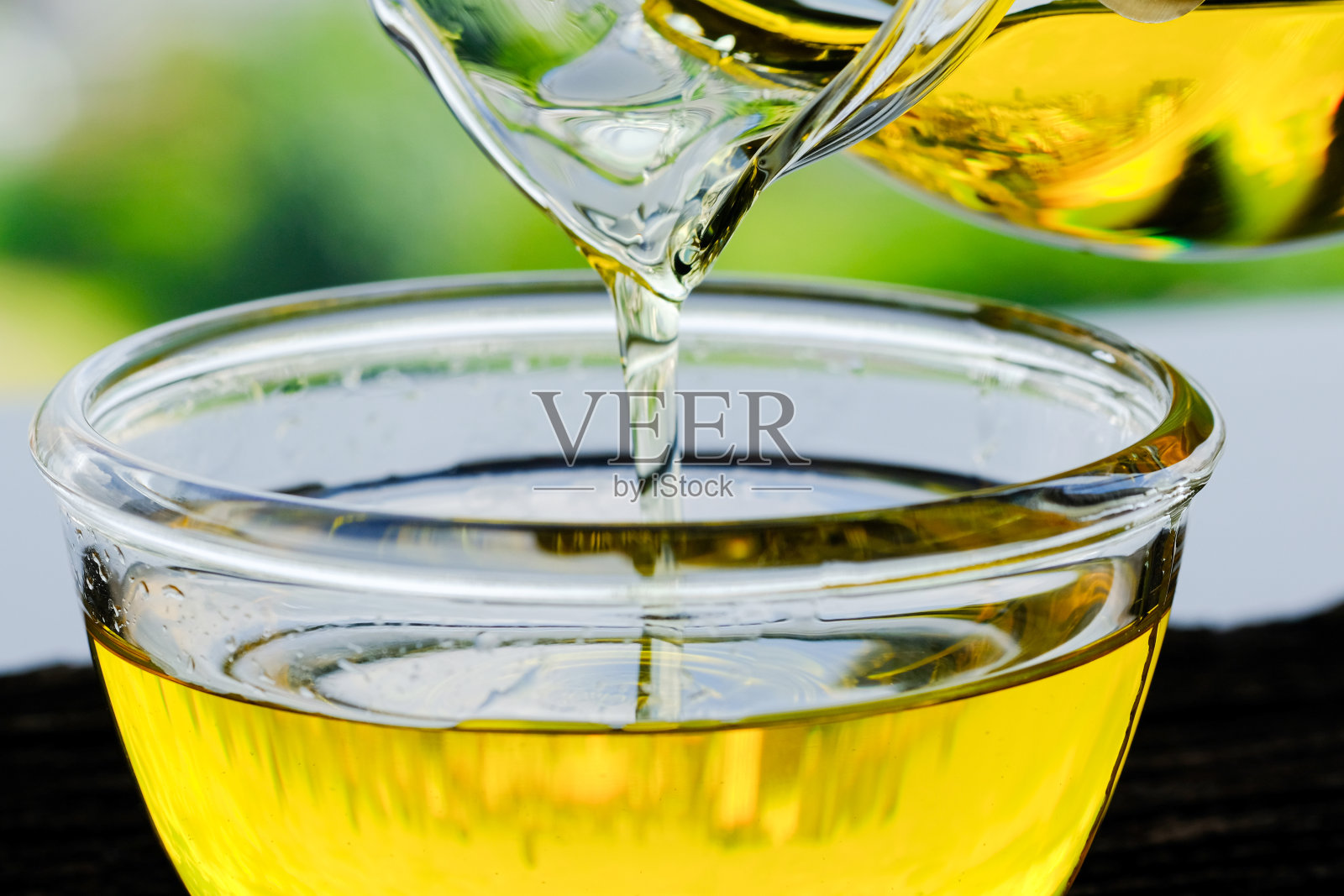 在石头厨房的玻璃碗里倒入橄榄油，里面有绿色的花园景观。准备烹饪概念。保健和美容概念。照片摄影图片