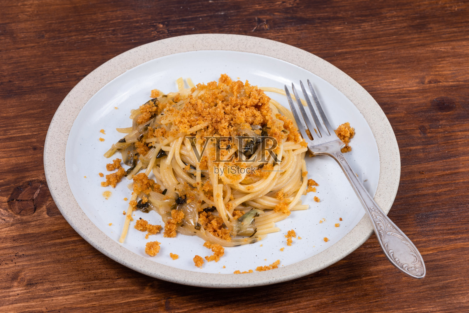 意大利细面条，一盘加洋葱和面包屑的意大利面，放在质朴的木桌上照片摄影图片
